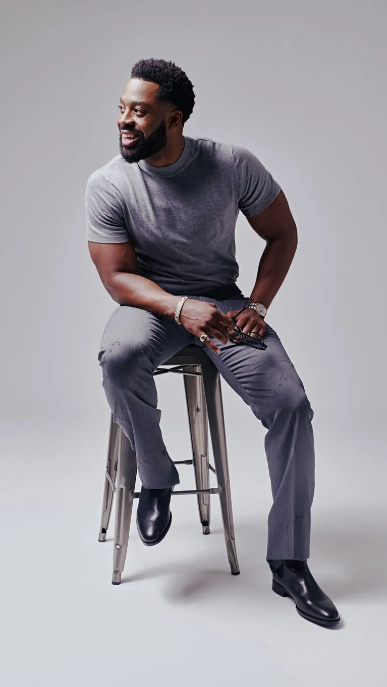 LaRoyce seated on a metal stool in a grey T-shirt and trousers